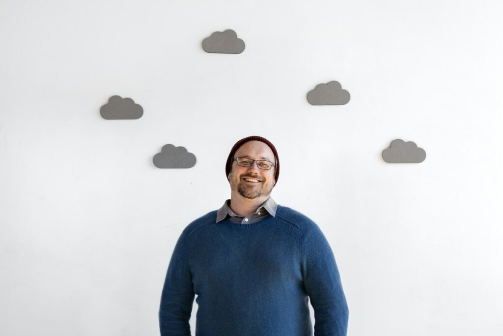 Hombre sonriente de frente en una pared blanca con nubes grises, representando a un líder de opinión. 