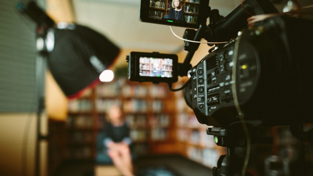 Mujer en una biblioteca grabando un video promocional para su página web. 